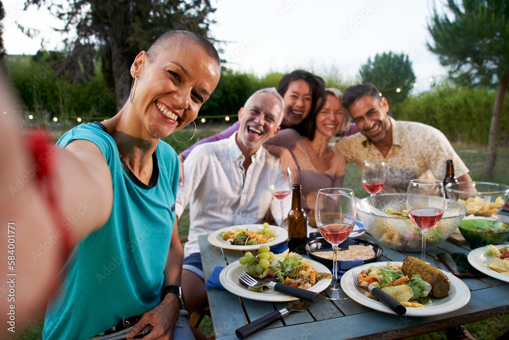 Group of friends taking selfie at barbecue dinner time. Middle-aged people chilling outside eating and drinking on patio terrace home. Food and friendship concept. High quality photo