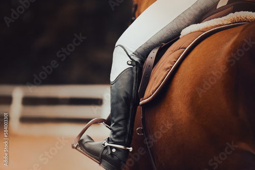 Rear view of a rider sitting in the saddle on a bay horse. Equestrian sports and ammunition. Stirrups. Horse riding.