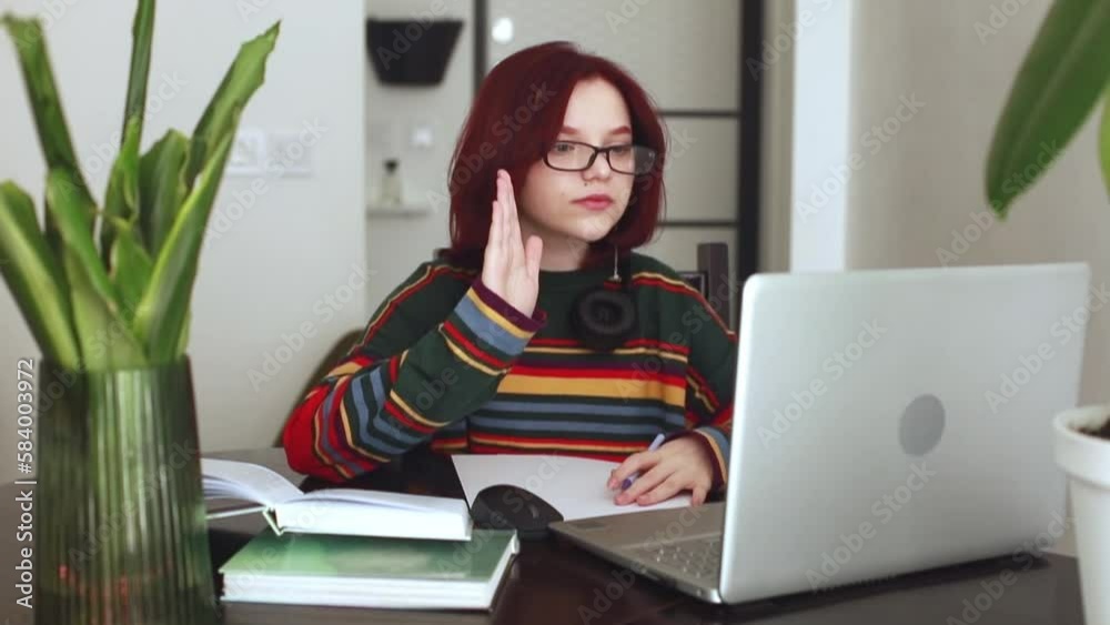A girl with red hair, a teenager of 15 years old with glasses, works at a laptop, online learning, a conference. Online learning concept A girl with red hair, a teenager of 15 years old with glasses, works at a laptop, online learning, a conference. Online learning concept