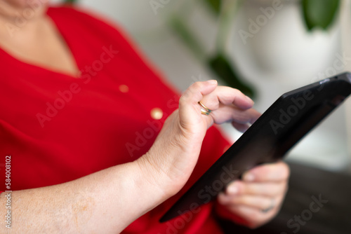 The world in the palm of her hand  elderly woman sitting on sofa using tablet  close-up