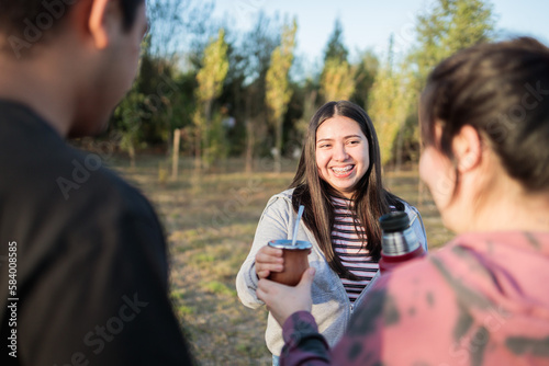 Group of smiling friends drinking yerba mate using a thermo with hot water in the countryside at sunset. photo