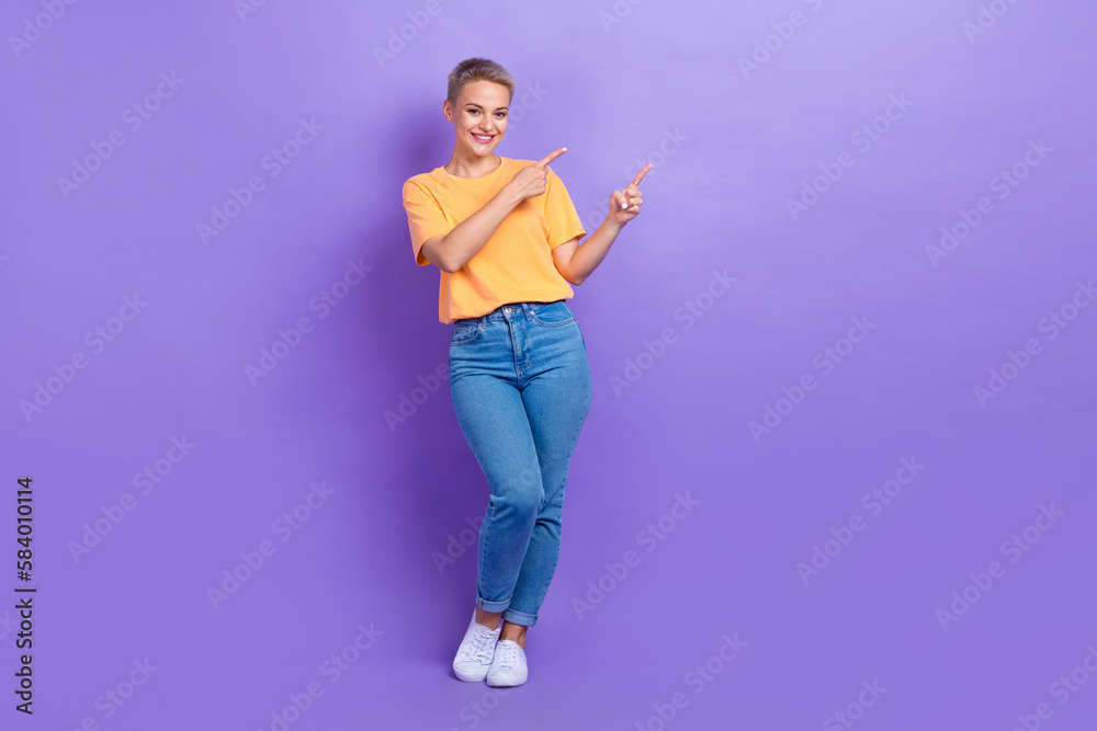 Full size photo of satisfied adorable girl dressed sneakers denim pants indicating empty space isolated on purple color background