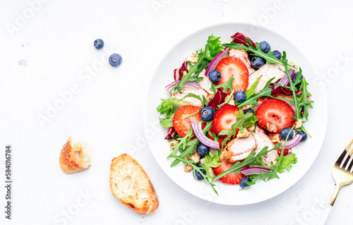 Strawberry, grilled chicken fillet and herbs healthy salad with arugula, blueberries and walnuts, white kitchen table, place for text. Fresh useful dish for healthy eating