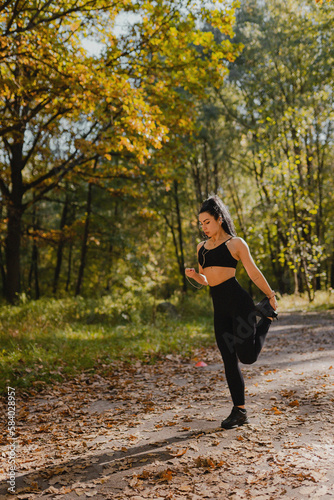 Fototapeta Naklejka Na Ścianę i Meble -  A young girl with black hair with a beautiful athletic figure goes in for sports in the morning while jogging in an autumn forest dotted with yellow leaves