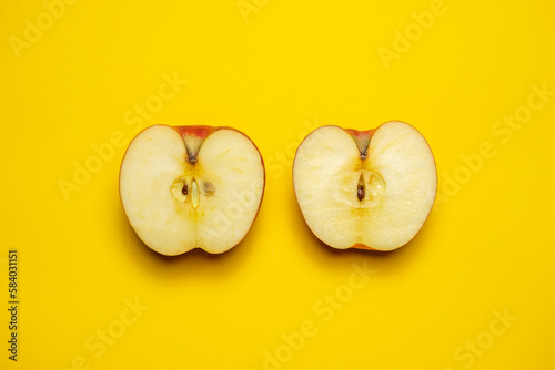 A juicy organic red apple cut in half on a yellow background. Cool minimal flat lay, copy space (ID: 584031151)