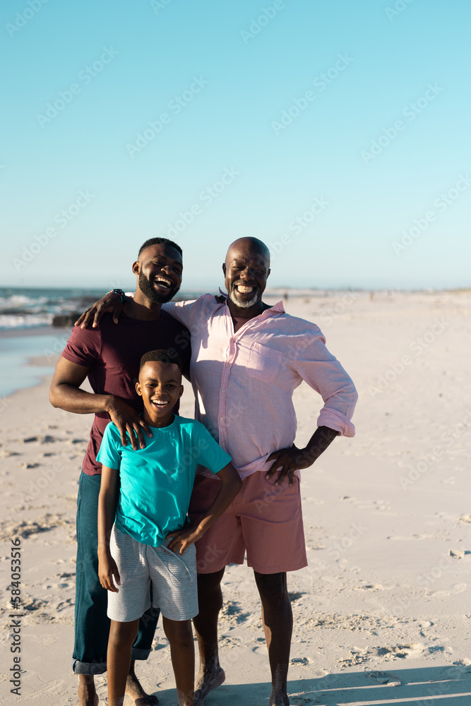 African american male multigeneration family laughing cheerfully and standing at beach under sky