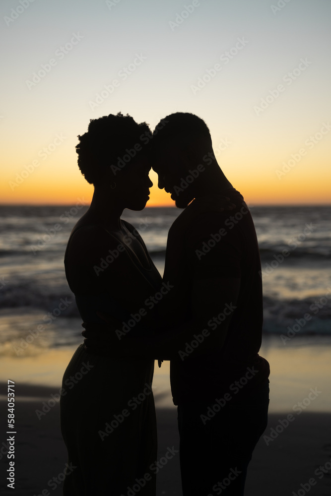 Naklejka premium Silhouette african american romantic couple with head to head standing against sea and clear sky