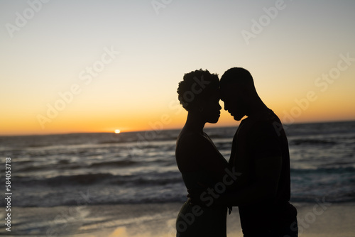 Silhouette african american romantic couple with head to head standing at beach during sunset