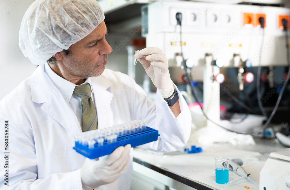 Fototapeta premium Adult man scientist in a medical gown conducts experiments with liquids in the laboratory