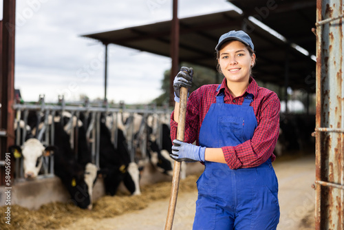 Foto Hardworking young woman farmer in overalls posing with rake and smiling at camer