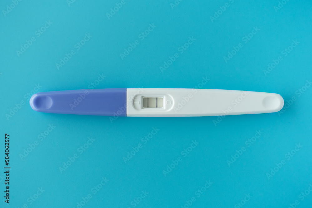 White Plastic Pregnancy test positive with two stripes results isolated on Pastel light blue background. Closeup. Top down view.