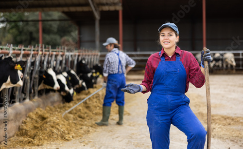 Young female farmer posing against backdrop of feeding cows on dairy farm