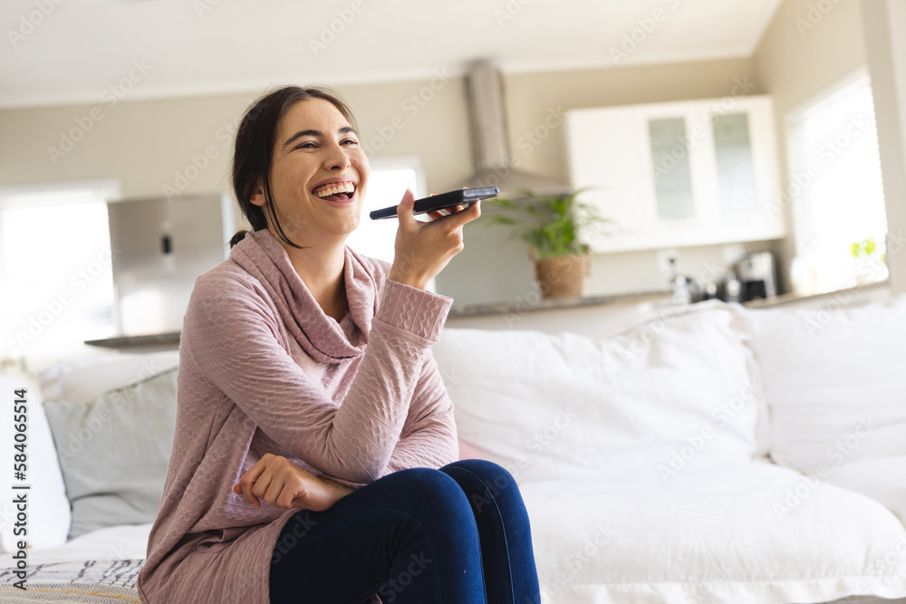Cheerful caucasian young woman talking on speaker over mobile phone while sitting on sofa at home Cheerful caucasian young woman talking on speaker over mobile phone while sitting on sofa at home