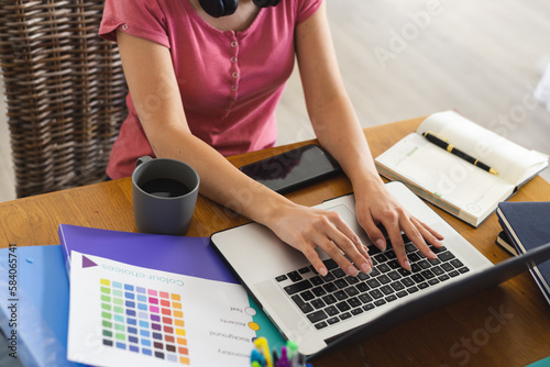Midsection of caucasian young woman with color swatch and files working over laptop on table photo