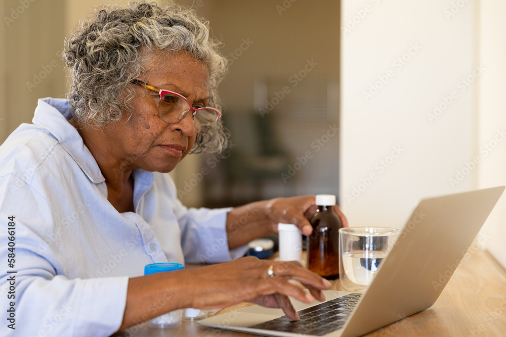 African american senior woman with prescription bottles using laptop on table at home African american senior woman with prescription bottles using laptop on table at home