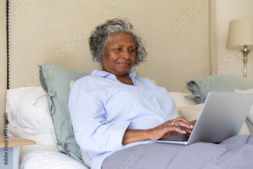 Focused african american senior businesswoman working over laptop while sitting on bed, copy space photo