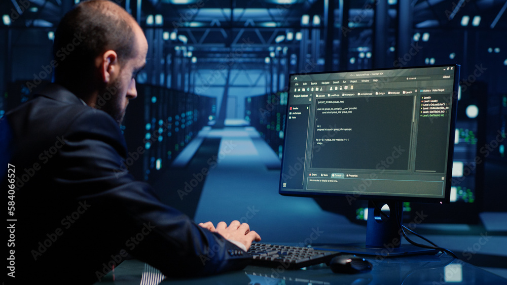 Male system engineer analyzing big data on computer, checking cloud computing network and digital servers. Young IT technician inspecting modern data center for digitalization. Handheld shot. Male system engineer analyzing big data on computer, checking cloud computing network and digital servers. Young IT technician inspecting modern data center for digitalization. Handheld shot.