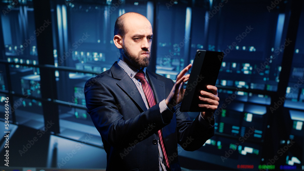 Fototapeta premium Datacenter engineer looking at mainframe diagnostics using digital tablet, inspecting cloud computing server room. IT infrastructure specialist working with fintech in data center.