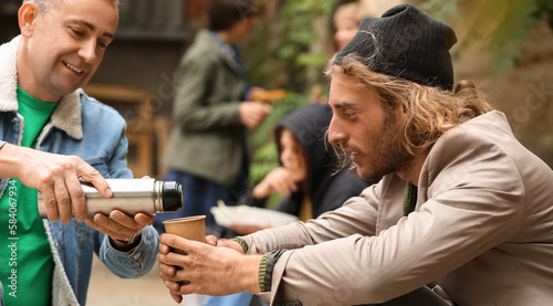 Volunteer giving drink to homeless man outdoors