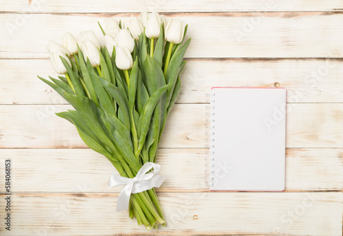White tulip bouquet with notebook on wooden background  top view