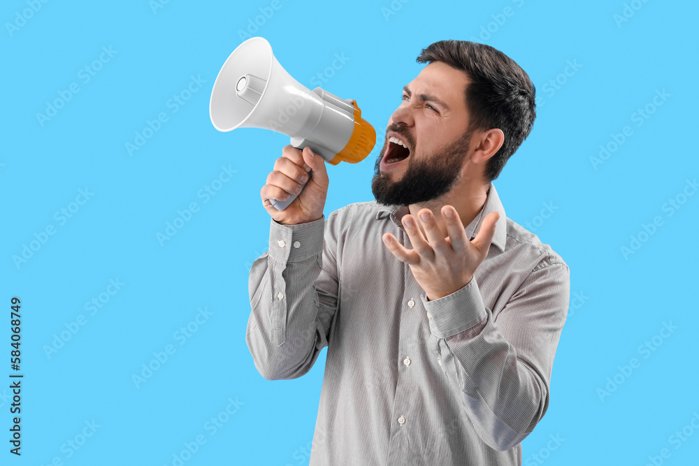 Angry young man shouting into megaphone on blue background Angry young man shouting into megaphone on blue background
