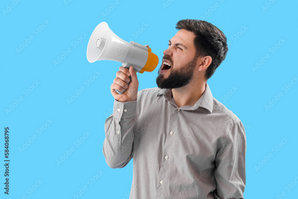 Angry young man shouting into megaphone on blue background Angry young man shouting into megaphone on blue background