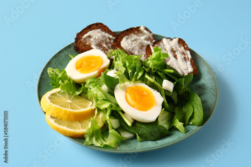 Plate of delicious salad with boiled eggs and cream cheese sandwiches on blue background