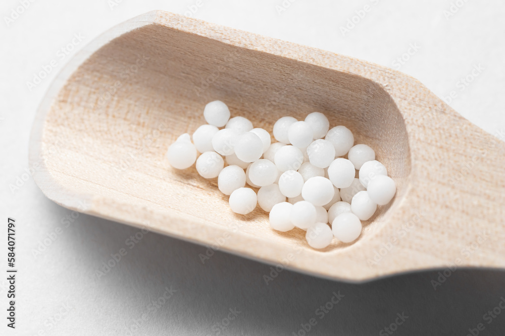 White homeopathic granules on a small wooden scoop