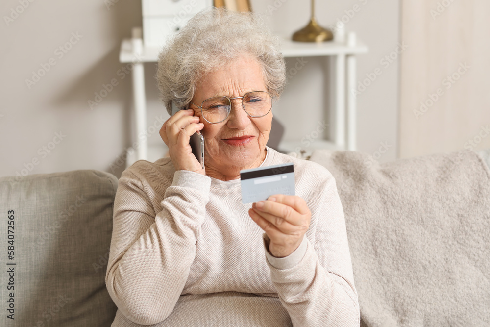 Senior woman with credit card talking by mobile phone on sofa at home Senior woman with credit card talking by mobile phone on sofa at home