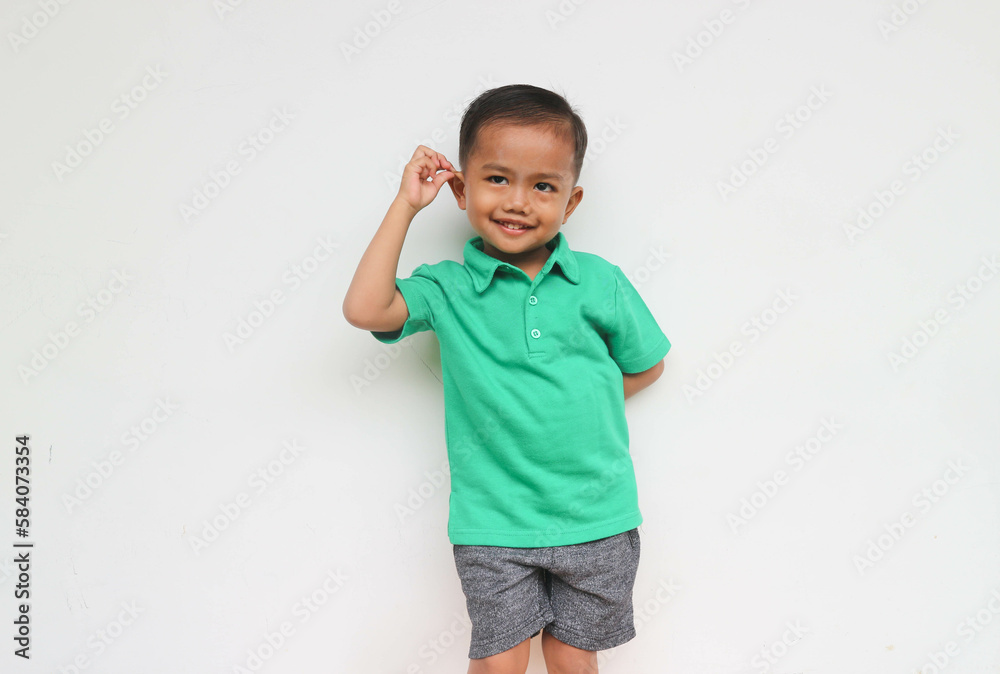 Portrait of a cute little asian boy smiling while holding his ear looking at camera, isolated on the white background Portrait of a cute little asian boy smiling while holding his ear looking at camera, isolated on the white background