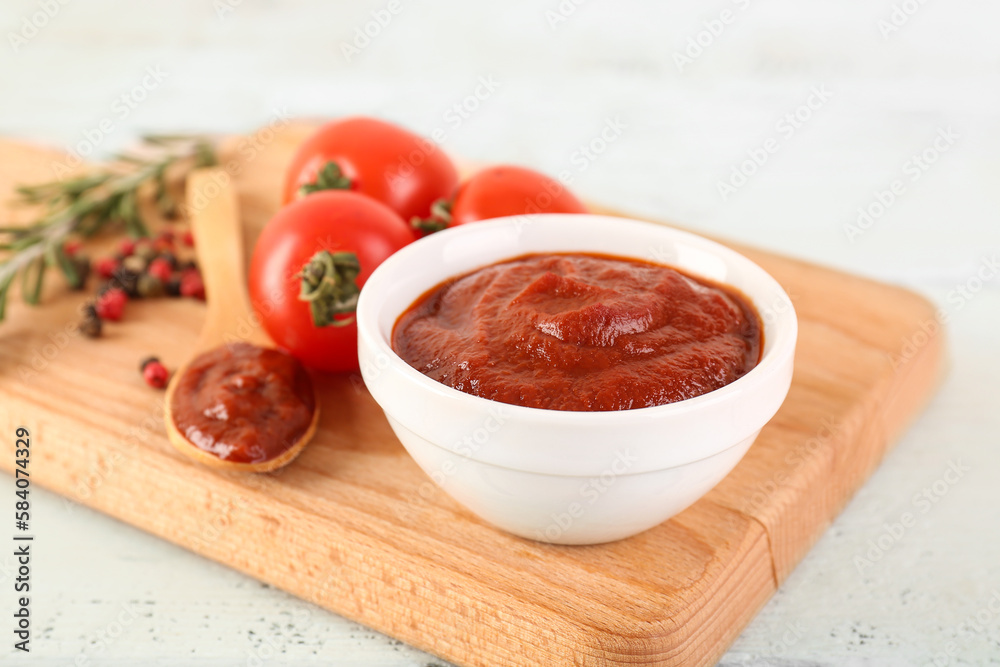 Board with bowl and spoon of tasty tomato paste on white wooden background Board with bowl and spoon of tasty tomato paste on white wooden background