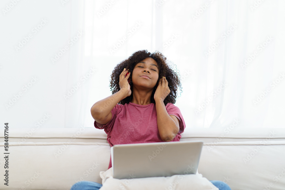 American - African black young woman sitting on sofa in living room and enjoy watching a social media on laptop computer in free time. American - African black young woman sitting on sofa in living room and enjoy watching a social media on laptop computer in free time.