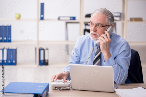 Old male employee speaking by phone in the office