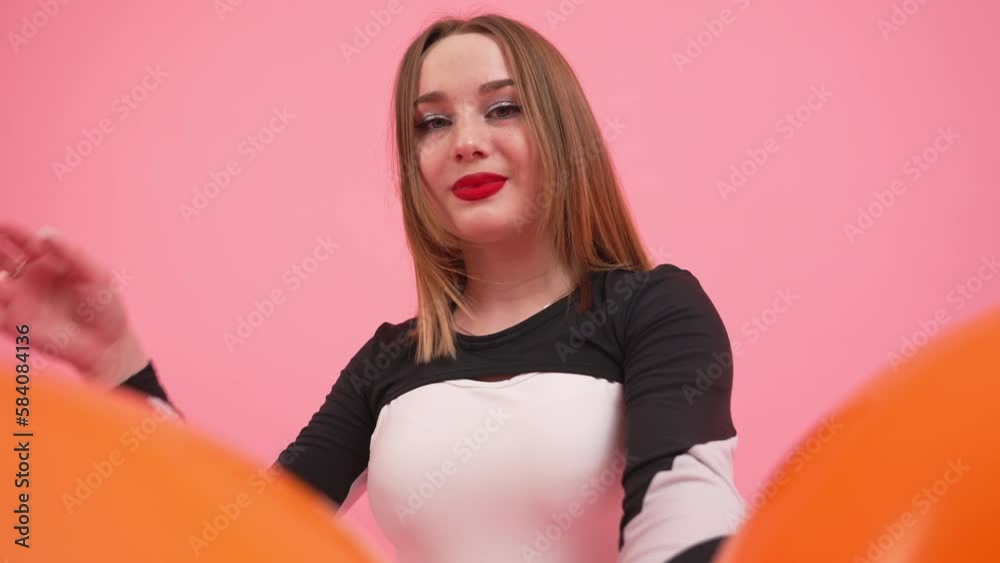 Low angle shot of young woman holding orange air balloons on pink background. High quality 4k footage Low angle shot of young woman holding orange air balloons on pink background. High quality 4k footage