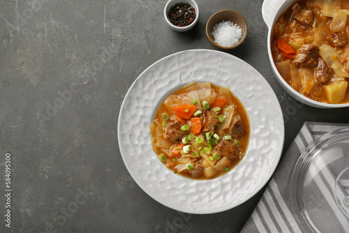 Tasty cabbage soup with meat, green onion and carrot served on grey table, flat lay. Space for text