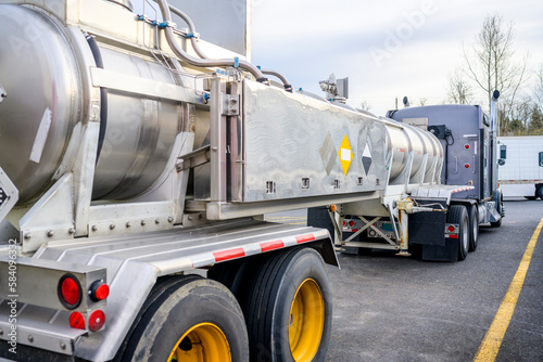 Professional industrial big rig semi truck with a tank semi trailer for transporting toxic chemicals standing on the truck stop parking lot