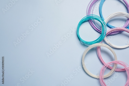 Colorful plastic filaments for 3D pen on light blue background, flat lay. Space for text