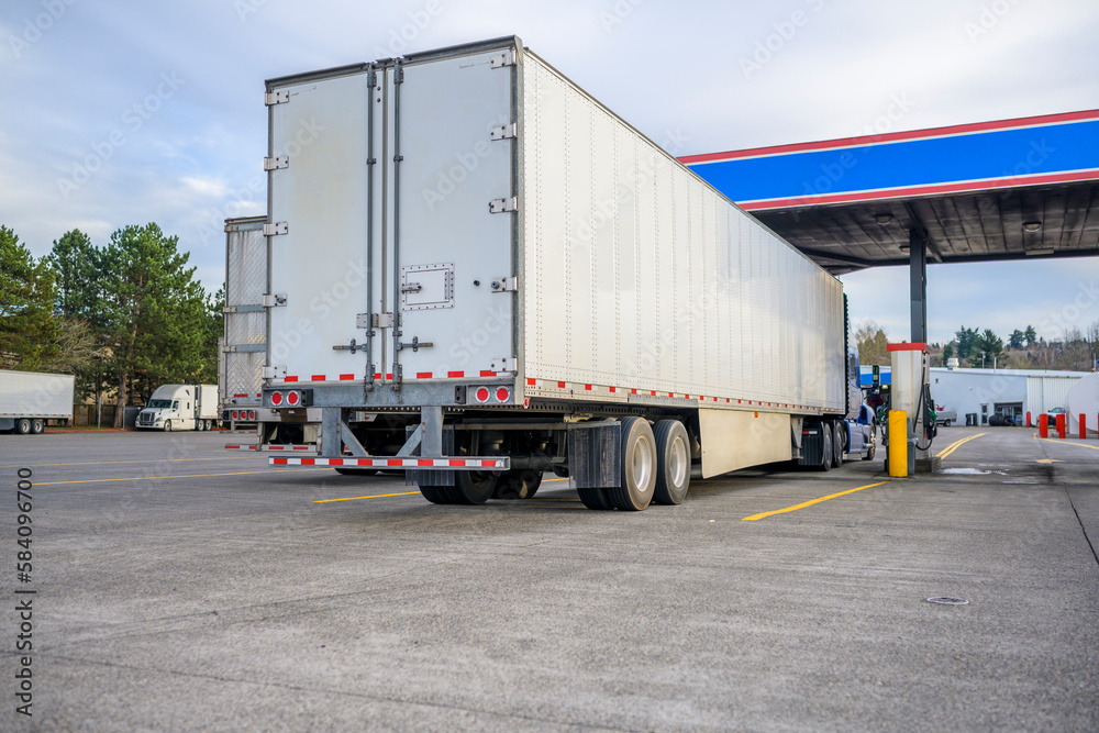 Row of the big rigs semi trucks with semi trailers filling tanks with diesel fuel standing on the fuel station on truck stop parking lot Row of the big rigs semi trucks with semi trailers filling tanks with diesel fuel standing on the fuel station on truck stop parking lot