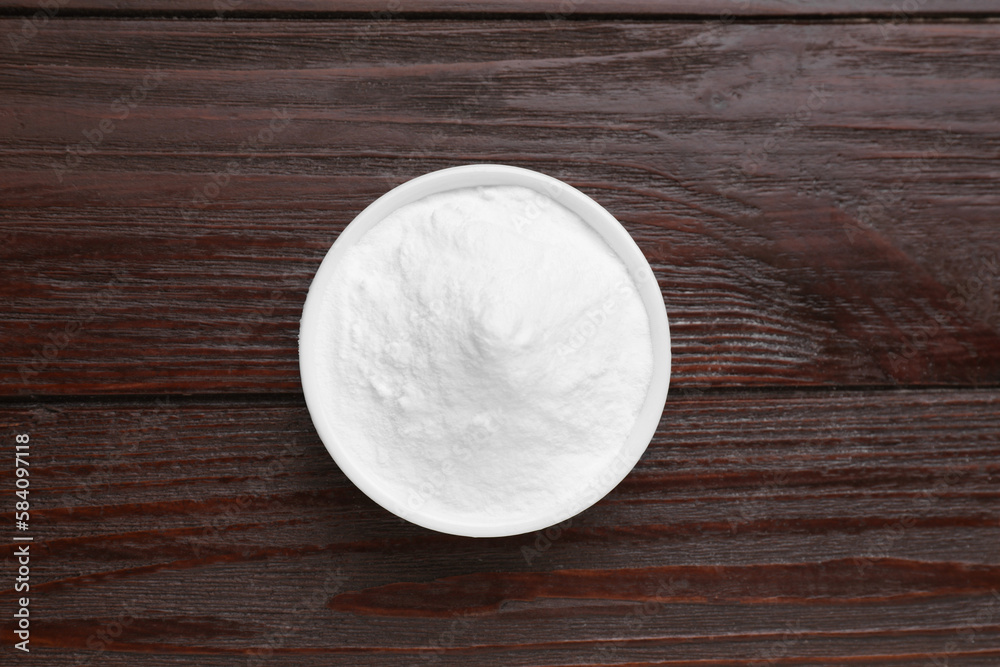 Bowl of sweet powdered fructose on black wooden table, top view
