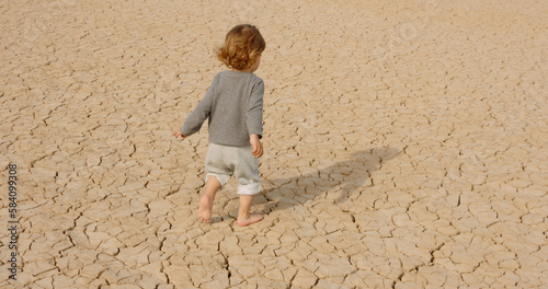  Funny caucasian baby boy running on deserted ground. Cracked soil land after erosions and desertification - ecology, save our planet concept 