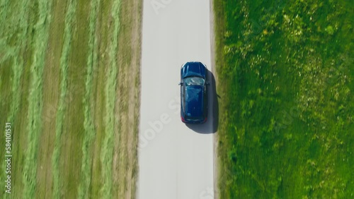 Topshot of a blue BMW car driving through countryside, surrounded by green meadows in breathtaking drone footage. Ideal for auto ads and travel vlogs. photo