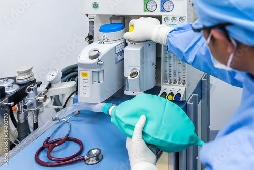 Anesthesiologist or doctor in blue gown working with anesthetic machine inside operating room in hospital.Right hand control machine with ambu bag.Medical device for surgery.Gas exchange control. photo