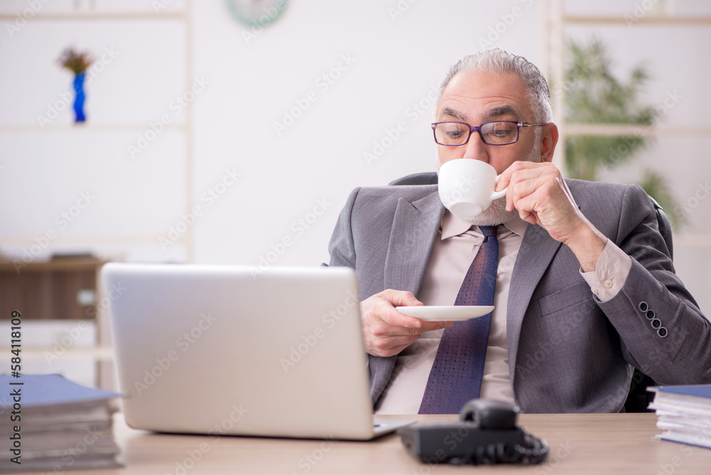 Old male employee drinking coffee in the office Old male employee drinking coffee in the office