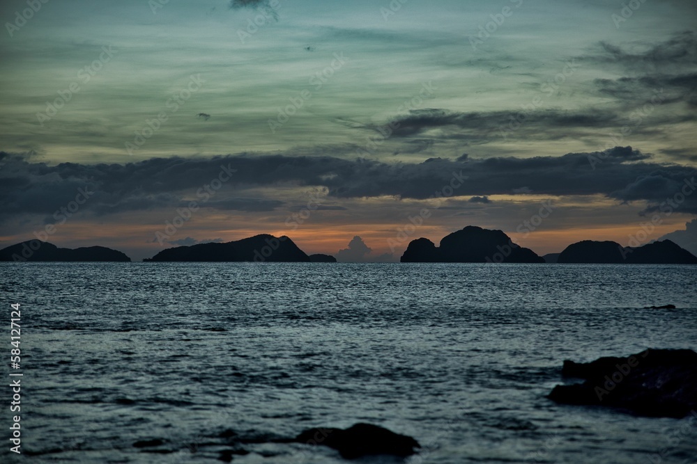 Picturesque sunset at the sea of El Nido, Palawan in the Philippines, the sky shines in golden orange and yellow tones, hills in the background.