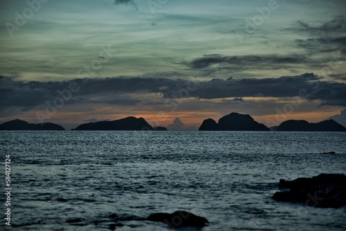 Picturesque sunset at the sea of El Nido, Palawan in the Philippines, the sky shines in golden orange and yellow tones, hills in the background.