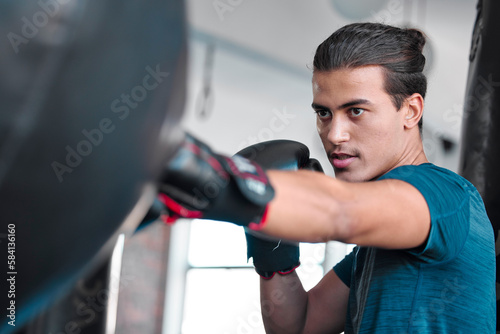 Fitness, serious man and boxing for exercise, workout or practice training at the gym for fight. Active and focused male boxer hitting punching bag with gloves for intense sports or fighting skill