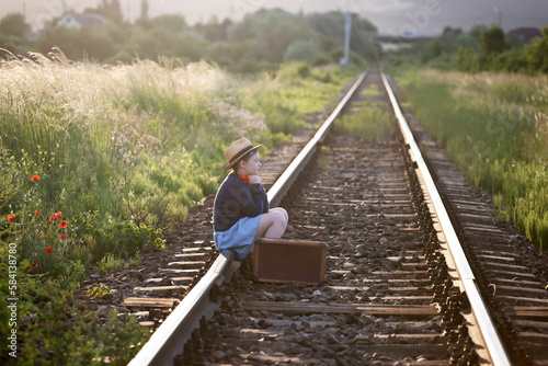 A little girl in a dress sits on an abandoned railroad tracks