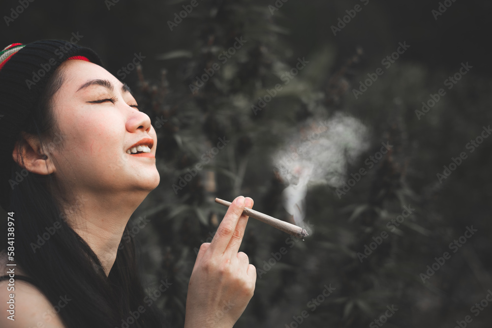 Obraz premium Yong Asia woman smoking marijuana at cannabis tree plant background