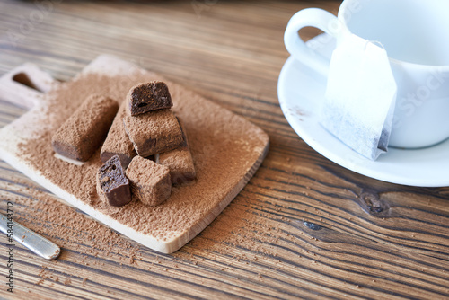 A cup and saucer and a tea bag with candy sprinkled with cocoa. A sweet snack, a time of pause.