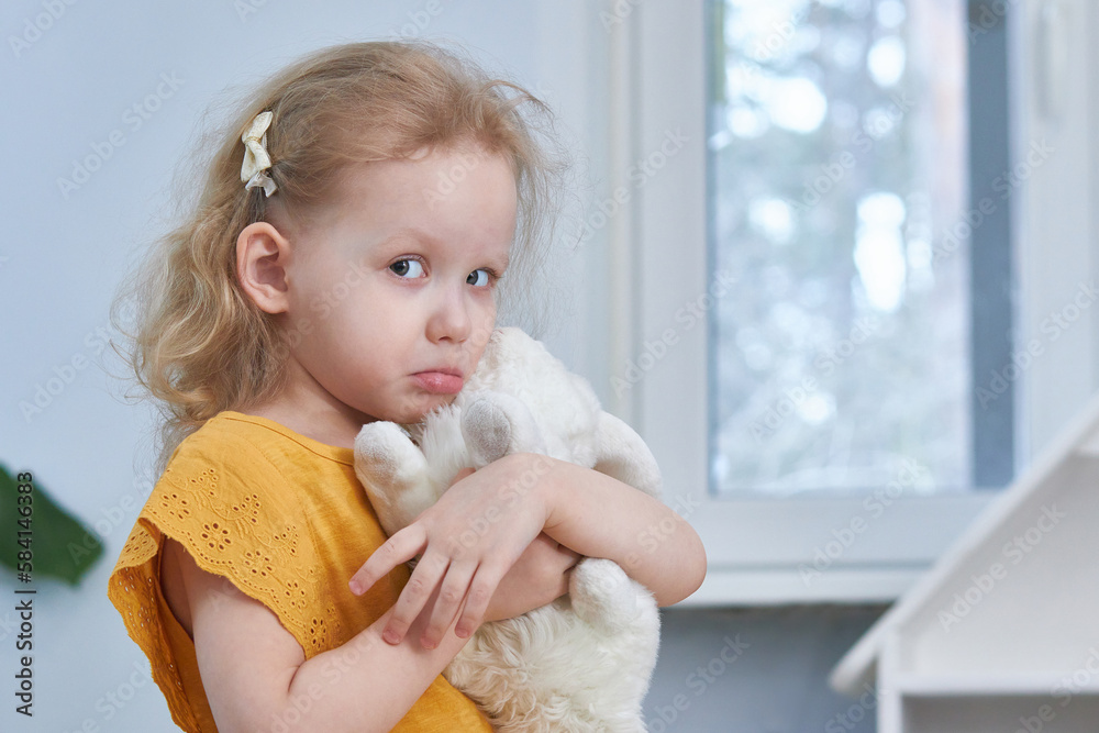 An offended girl hugs a white rabbit toy. Copy Space. An offended girl hugs a white rabbit toy. Copy Space.